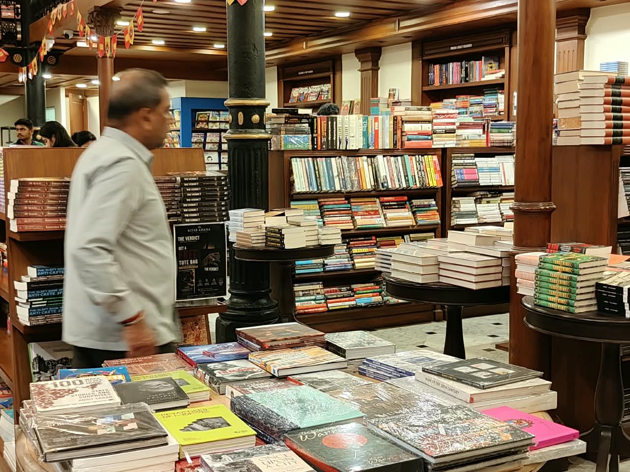 A man walking past tables of books in a wood panelled bookshop